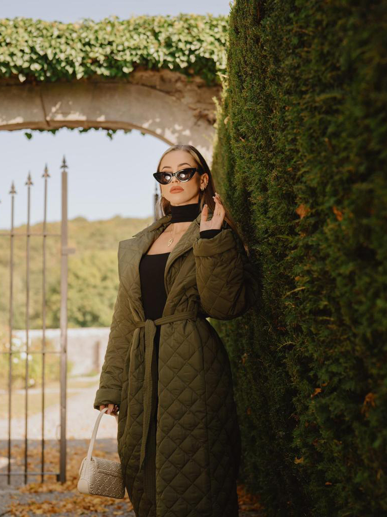 Fille près d'un buisson avec un manteau kaki et des lunettes de soleil